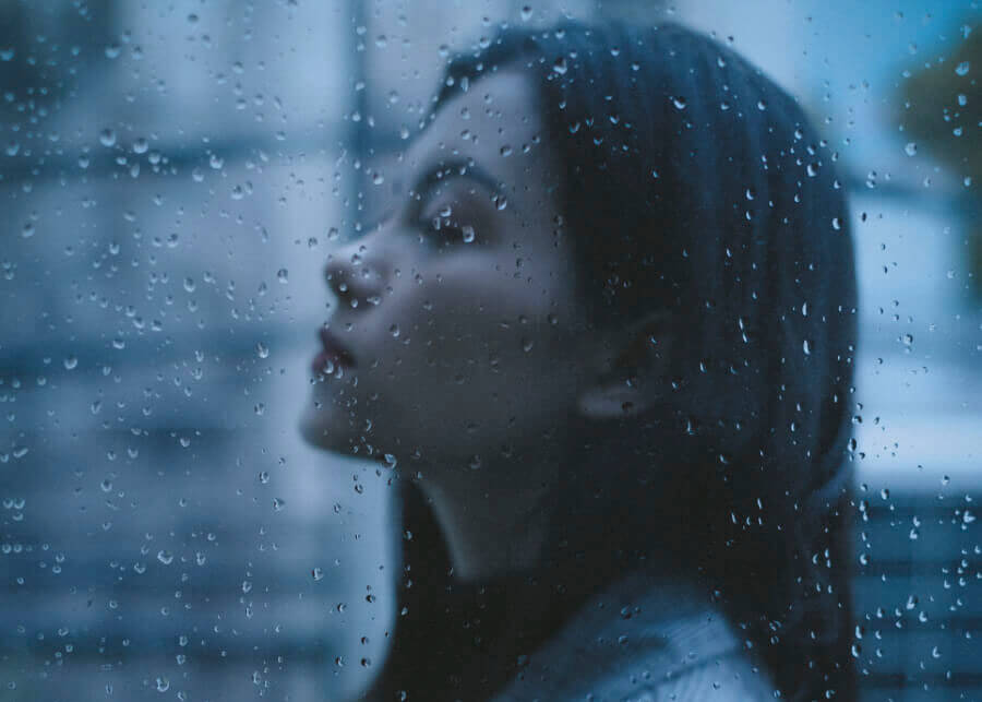 Photo grise d'une femme de profil derrière une vitre mouillée